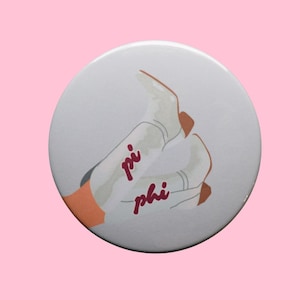 May include: White button with a graphic of two white cowboy boots with brown accents and the words "pi phi" in red script. The button is set against a pink background.