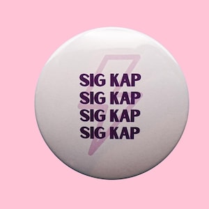 May include: A white button with the text "SIG KAP" stacked four times in a dark purple font. A light purple lightning bolt graphic is centered above the text. The background is a solid light pink.
