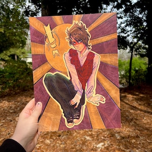 May include: An art print featuring a stylized illustration of a person in a red vest and white shirt, with a background of a sunburst design in gold and purple. The person is wearing dark pants and sneakers. The artwork has a vintage aesthetic.