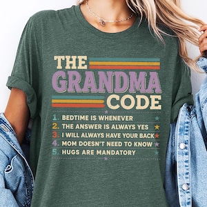 Op de afbeelding: Groen t-shirt met de tekst "THE GRANDMA CODE" in een retro-ontwerp. De tekst bevat de regels: "BEDTIME IS WHENEVER", "THE ANSWER IS ALWAYS YES", "I WILL ALWAYS HAVE YOUR BACK", "MOM DOESN'T NEED TO KNOW" en "HUGS ARE MANDATORY".