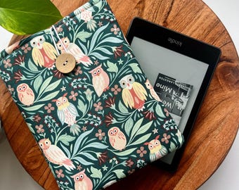 May include: A green fabric Kindle cover with a floral pattern featuring owls. The cover has a button closure and the text "Kindle" is visible on the e-reader.
