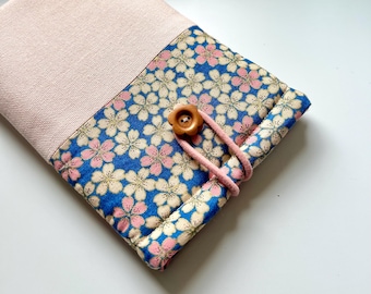 Puede incluir: Una pequeña bolsa de tela rosa y azul con un patrón floral y un cierre de botón de madera.
