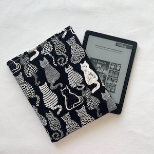 May include: Black and white cat print e-reader cover with a black e-reader inside. The e-reader screen shows the text "History always has something to hide. Can DS Karen Hart unravel the truth?" and the title "In Plain Sight" by D.S. Butler.