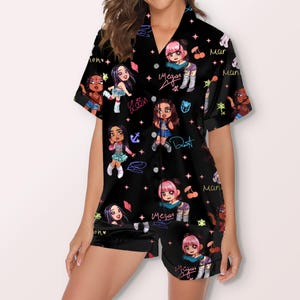 May include: Black pajama set with a repeating pattern of cartoon characters, signatures, and stars. The short-sleeved top and shorts feature a black background with colorful illustrations. The characters have various hairstyles and outfits.