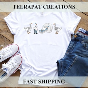 May include: White t-shirt with a humorous graphic featuring geese in medical scenarios. The design includes geese with skeletal outlines, a doctor goose, and an MRI machine. The text "TEERAPAT CREATIONS" and "FAST SHIPPING" are printed on the shirt.