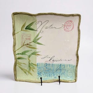 May include: A square ceramic plate with a wavy gold-toned rim. The surface features a light green panel with painted bamboo stalks, a cream-colored section with the script text Nature and Les Papillons, and a blue base with red stamp motifs.