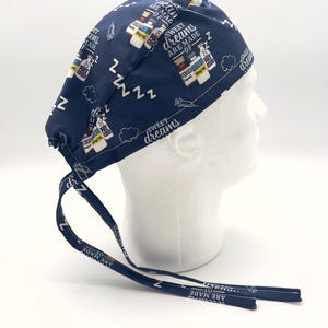 Op de afbeelding: Blauwe chirurgische scrub-muts met een witte print van medicijnflesjes, spuiten en de tekst "Sweet dreams are made of ZZZ".