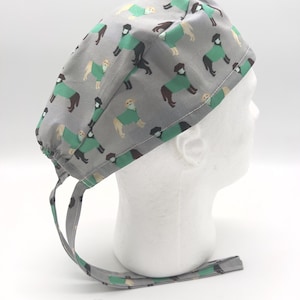 May include: A gray surgical scrub hat with a pattern of dogs wearing green scrubs. The hat has two long ties.