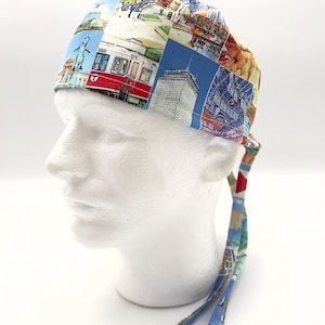 May include: A blue, white, and red patterned surgical scrub hat with long ties. The pattern features images of a city skyline, a train, and other urban scenes.