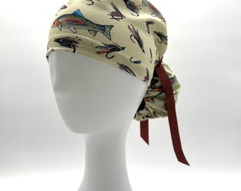 May include: A beige surgical scrub cap featuring a colorful fish and fly pattern. The cap is tied in the back with a brown ribbon. The cap is designed to be worn by medical professionals or anyone needing to cover their hair.