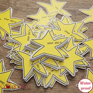 Op de afbeelding: Een stapel gele ster-vormige stickers met zwarte randen en de tekst "your did it". De stickers zijn waterdicht.