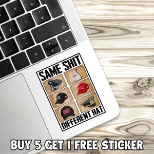 Puede incluir: Una pegatina blanca en un port&aacute;til con el texto "SAME SHIT DIFFERENT HAT" e im&aacute;genes de diferentes sombreros. La pegatina tambi&eacute;n tiene el texto "BUY 5 GET 1 FREE STICKER". El port&aacute;til est&aacute; sobre una superficie de madera.