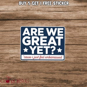 May include: A navy blue sticker with white text that reads "ARE WE GREAT YET?" with stars. Below the main text is the phrase "'cause i just feel embarrassed" in white text on a red background.