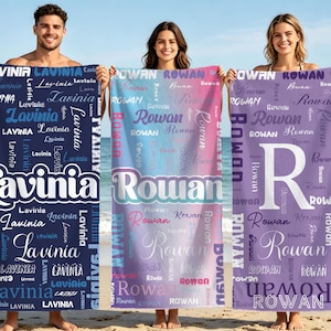 May include: Three personalized beach towels with names printed on them. One is navy blue with the name "Lavinia" in white, another is a gradient of pink and blue with the name "Rowan", and the third is purple with the name "Rowan".