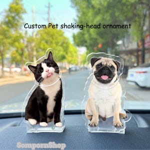 May include: Two clear acrylic pet ornaments. One features a black and white cat with its tongue out, and the other a beige pug with its tongue out. The text "Custom Pet shaking-head ornament" is above the ornaments.