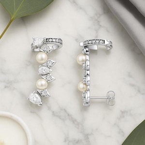 Puede incluir: Elegantes pendientes plateados con diseño en forma de pera, gemas transparentes y perlas. Los pendientes tienen una disposición en cascada delicada, con una pequeña banda de gemas en la parte superior. El diseño es refinado.