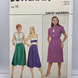 Op de afbeelding: Vintage Butterick naaipatroon, maat 10, met illustraties van drie jurk ontwerpen. Het patroon toont een jurk met een groene rok en witte top, een paarse jurk met witte strepen en een paarse jurk met bijpassend jasje.