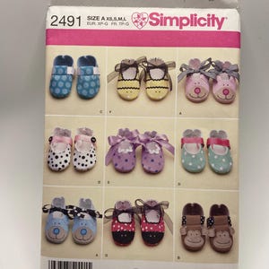 Pode incluir: Padrão Simplicity 2491 para sapatos de bebé. O padrão inclui vários designs de sapatos, incluindo bolinhas, rostos de animais e laços. A embalagem é rosa e branca com o logotipo Simplicity e uma etiqueta de preço.