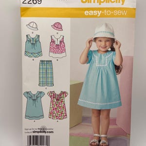 Könnte beinhalten: Simplicity Schnittmuster 2269 für Mädchenkleidung. Das Muster enthält Designs für Kleider, Oberteile, Hosen und einen Hut. Das Cover zeigt ein junges Mädchen in einem blauen Kleid und Hut. Der Text "easy-to-sew" ist zu sehen.