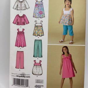 Könnte beinhalten: Simplicity leicht zu nähendes Schnittmuster für Mädchenkleidung. Das Muster enthält Designs für Kleider, Oberteile und Hosen. Das Bild zeigt ein Mädchen mit einem floralen Oberteil und blauen Caprihosen. Ein weiteres Mädchen trägt ein rosa Kleid. Größe HH 3,4,5,6.