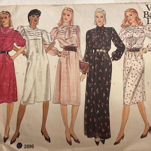 Peut inclure: Patron de couture vintage Vogue Basic Design présentant cinq modèles de robes. Les robes varient en style, dont une robe rouge à manches courtes, une robe blanche, une robe rose avec un nœud, une robe noire et une robe blanche à motifs floraux.