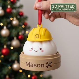 May include: A 3D printed ornament featuring a white dumpling character wearing a yellow construction hard hat with a house icon. The dumpling sits in a tan bamboo steamer base with the name Mason and a crossed hammer and wrench icon printed on it.