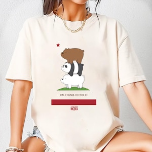 May include: Cream-colored t-shirt featuring a graphic of three cartoon bears stacked on top of each other. The bears are brown, panda-colored, and white. Below the bears is the text "CALIFORNIA REPUBLIC" and "BARE BEARS". A red star is above the bears.