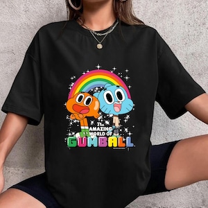 May include: Black t-shirt featuring a colorful graphic of characters from "The Amazing World of Gumball" cartoon. The design includes a rainbow, stars, and the show's title in a vibrant, multi-colored font. The shirt is a casual, unisex style.