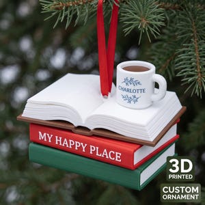 May include: A 3D printed ornament featuring a stack of two books with an open book on top and a white mug. The red book spine reads MY HAPPY PLACE in white text. The white mug features the name CHARLOTTE in blue with blue leaf accents.