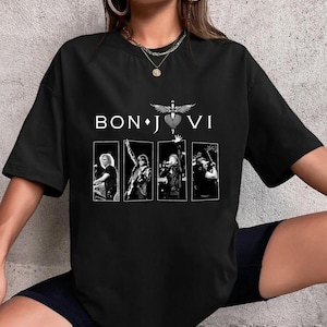 Op de afbeelding: Zwart T-shirt met de witte tekst "BON JOVI" boven vier zwart-wit afbeeldingen van de band. Het logo van de band, een hart met vleugels en een dolk, is gecentreerd boven de afbeeldingen.