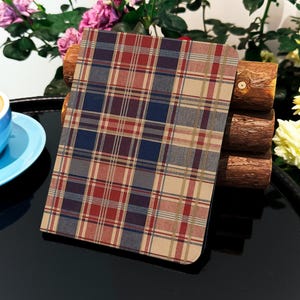 Może przedstawiać: Notatnik w kratę w kolorach czerwonym, niebieskim i beżowym. Leży na drewnianym stojaku. W tle niebieski filiżanka i spodek. Widoczne są również kwiaty.