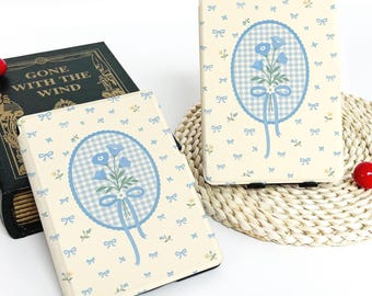 May include: Two cream-coloured e-reader covers with a floral design. Each cover features a blue gingham oval with a bouquet of blue flowers and a blue ribbon. The covers are decorated with small blue bows and flowers.