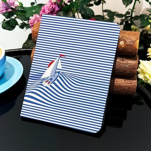 May include: A blue and white striped notebook cover with a sailboat graphic. The sailboat is white with red accents and is sailing on a wave.