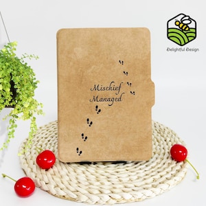 Puede incluir: Un cuaderno de papel kraft marrón con el texto "Mischief Managed" y un rastro de huellas en tinta negra. El cuaderno está sobre una estera de paja tejida.