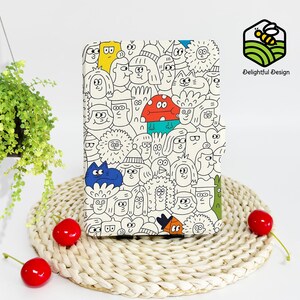 May include: A white Kindle e-reader cover with a black and white illustration of cartoon faces. The cover features a variety of characters with different expressions and hairstyles.