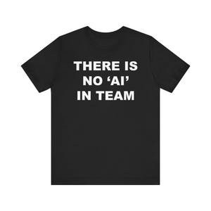 Puede incluir: Camiseta negra con el texto blanco "THERE IS NO 'AI' IN TEAM". La camiseta de manga corta está hecha de un material suave y tiene cuello redondo. El texto está centrado en la parte delantera de la camiseta.