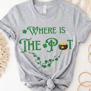 May include: A gray t-shirt with the text "Where is the Pot" in green, with a shamrock and a pot of gold graphic. The shirt is tied in a knot at the bottom.