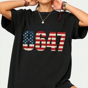 May include: Black t-shirt featuring the number "8647" in a distressed American flag design. The number "8" is filled with blue stars and white stripes, while the other numbers have red and white stripes. The shirt is a casual style.