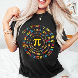 May include: Black t-shirt featuring a colorful design of the mathematical symbol Pi, surrounded by a spiral of numbers. The Pi symbol is yellow, and the numbers are in various colors. A casual, comfortable tee.