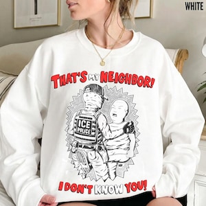 May include: White sweatshirt with a graphic illustration featuring two figures and the text "THAT'S MY NEIGHBOR! I DON'T KNOW YOU!" in red and black. The illustration depicts a person in an "ICE POLICE" vest and a child.