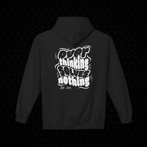 Puede incluir: Sudadera con capucha negra con texto blanco en la espalda que dice "Overthinking Solves Nothing" en una fuente estilizada. El texto incluye "Est. 2026" debajo de la frase principal. La sudadera tiene capucha y mangas largas.