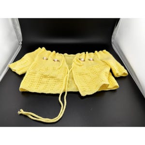 May include: A yellow knitted cardigan with short sleeves. The cardigan has a delicate floral embroidery on the chest and a drawstring closure. The garment is made of a soft, textured yarn, perfect for layering.