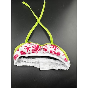 Op de afbeelding: Een witte bikinitop met rode bloemenprint en limoengroene randen en bandjes. De top heeft een herhalend patroon van rode bloemen en abstracte vormen. De bandjes kruisen elkaar op de rug.