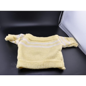 May include: A small, yellow knit sweater with white horizontal stripes on the sleeves and upper chest. The sweater has a ribbed hem and cuffs. The garment is made of a soft, textured yarn.