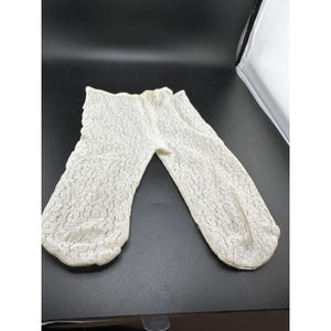 Può includere: Un paio di calzini alla caviglia in pizzo color bianco sporco con un delicato e intricato motivo floreale su tutto il tessuto. I calzini presentano un'apertura elastica a coste sulla parte superiore e una punta arrotondata, realizzati in materiale leggero e trasparente.