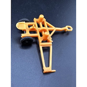 Könnte beinhalten: Ein orangefarbener Spielzeugtraktor aus Kunststoff mit zwei kleinen schwarzen Rädern. Das Spielzeug hat ein detailliertes Design mit verschiedenen geometrischen Formen und einem Anhängepunkt. Das Spielzeug ist wahrscheinlich eine Miniaturreplik eines landwirtschaftlichen Fahrzeugs.
