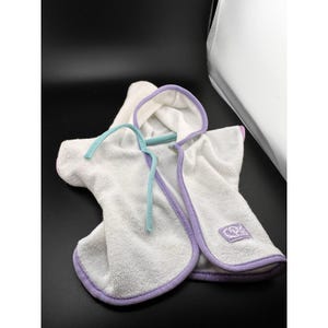May include: White hooded baby towel with a light blue drawstring and purple trim. The towel has a small square patch with a logo on the front. The towel is made of a soft, absorbent material.