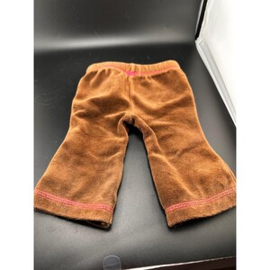 Könnte beinhalten: Braune Cordhose mit rosa Bund und rosa Nähten an den Säumen. Diese Hose ist für ein Kind konzipiert.