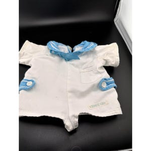 May include: White baby romper with blue sailor collar and accents. The romper has short sleeves, a small pocket, and blue accents on the cuffs. The romper has a tag that says "China Doll".