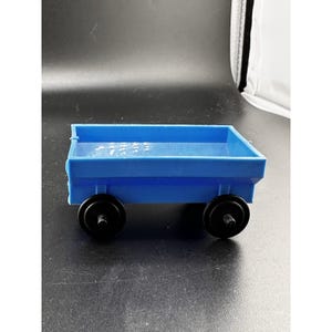 Könnte beinhalten: Ein kleiner, blauer Spielzeugwagen aus Kunststoff mit schwarzen Rädern. Die Wagenpritsche ist rechteckig und hat einen leicht erhöhten Rand. Die Räder sind rund und an der Unterseite des Wagens befestigt.